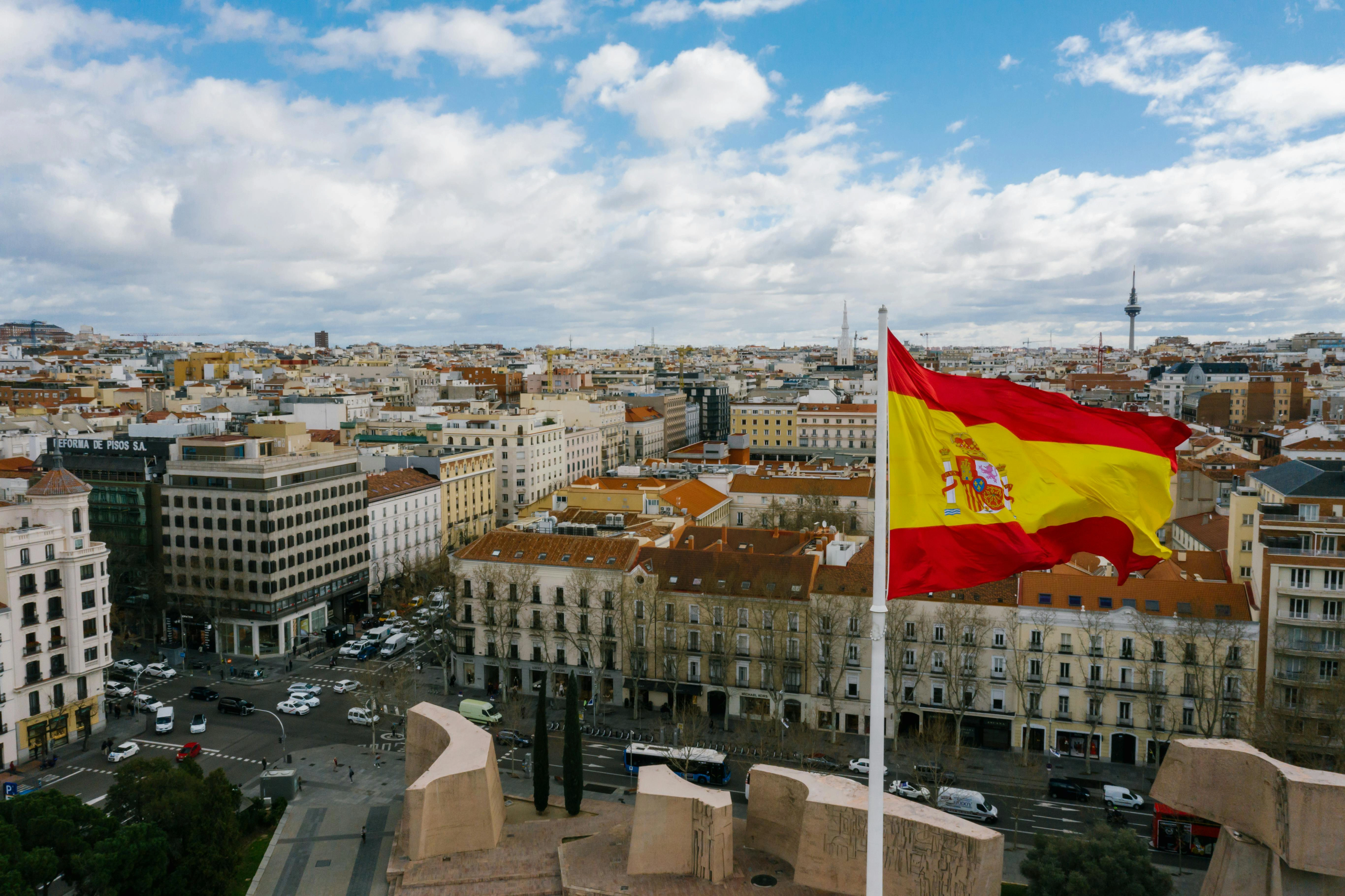 Spanische Flagge weht im Wind mit Stadt im Hintergrund - Hintergrund